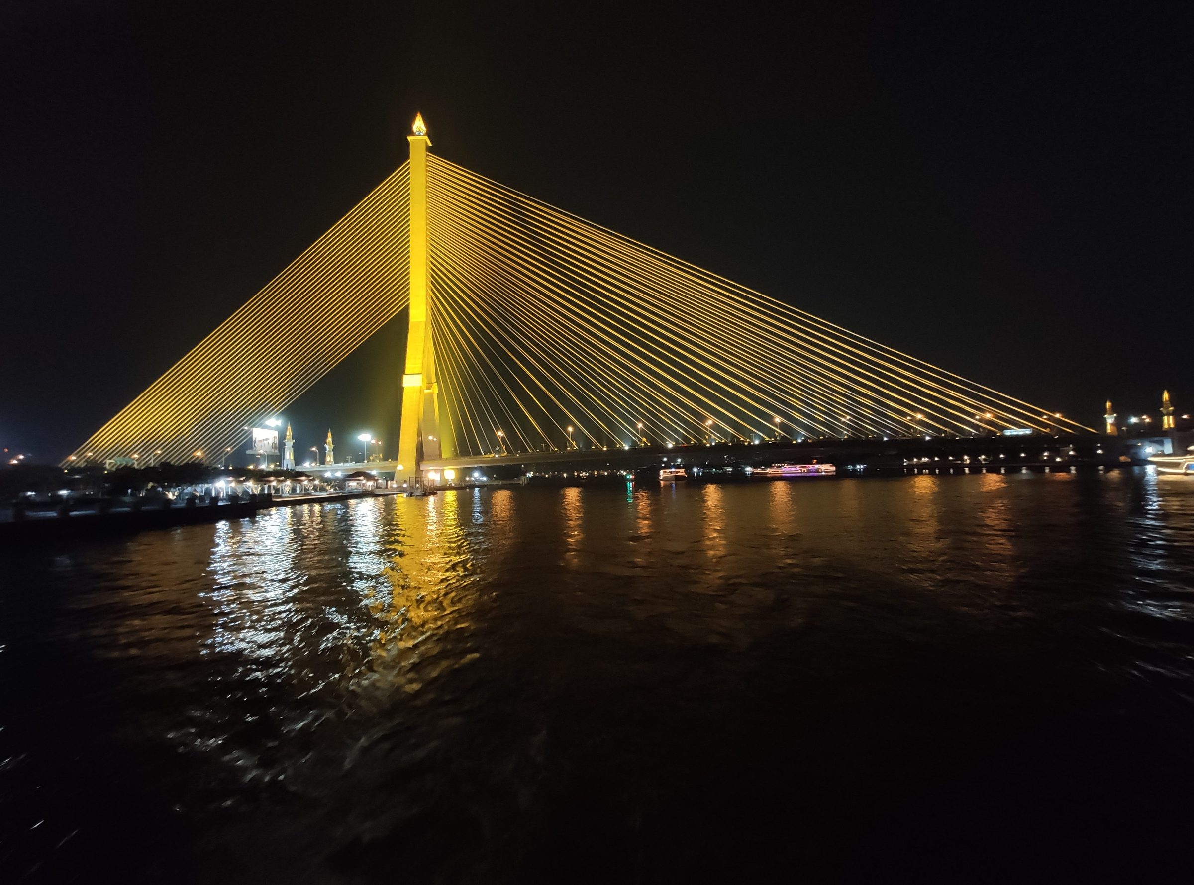 A cable-stayed bridge lit gold above a dark river at night