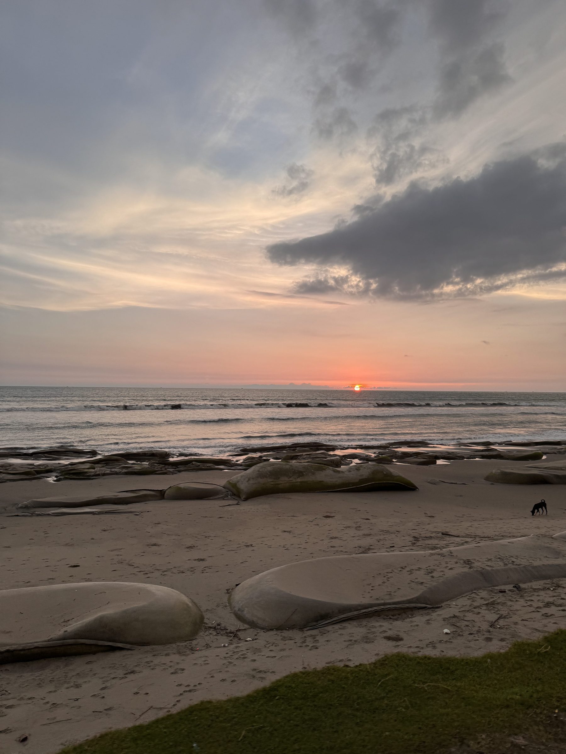 Rocks and sand at low tide under a cloudy sky as the sun sets