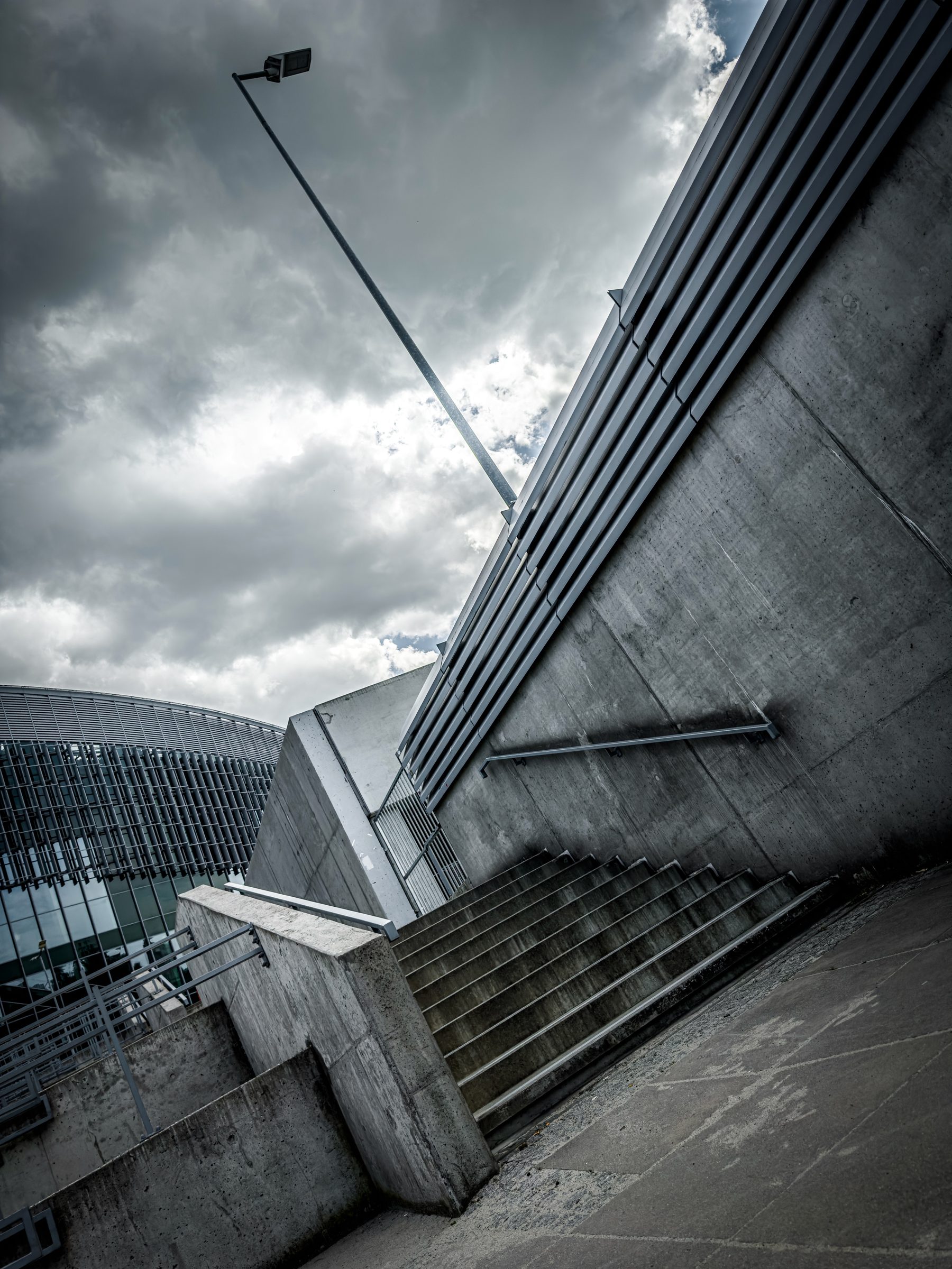Concrete stairs climbing beside a high concrete wall under a stormy sky