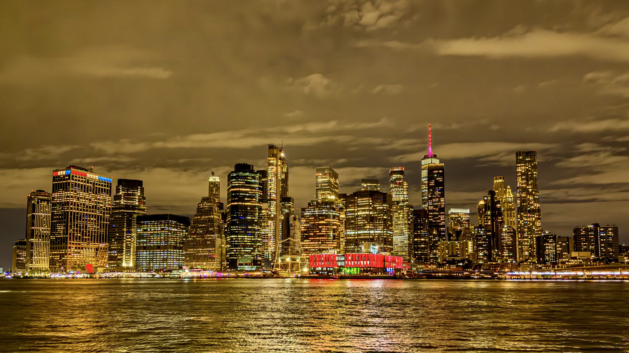 Skyscrapers lit gold at night across a river, reflected in the water