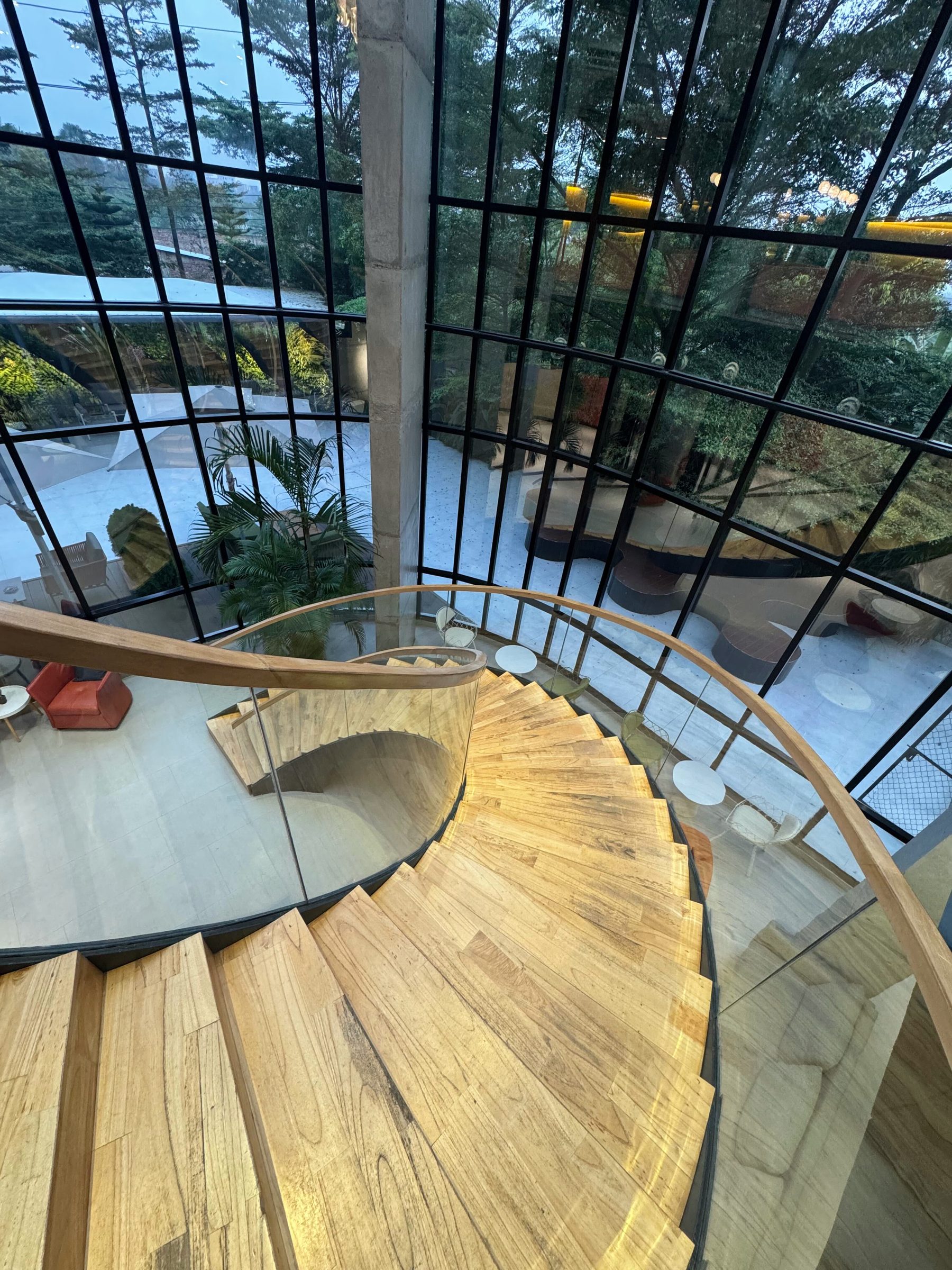 A wooden spiral stair with a glass rail, seen from above beside a gridded window