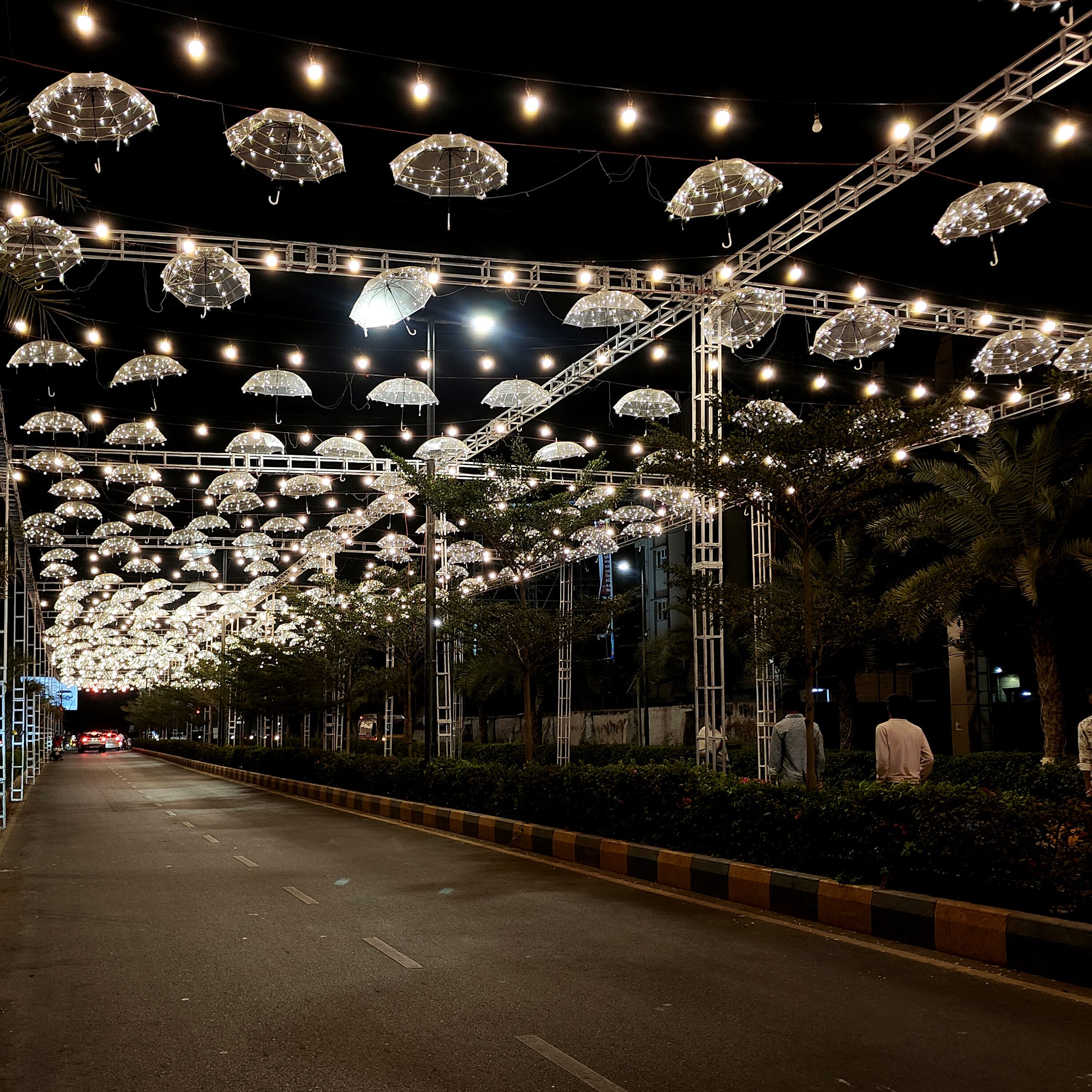 Lit umbrellas hanging in rows above an empty road at night