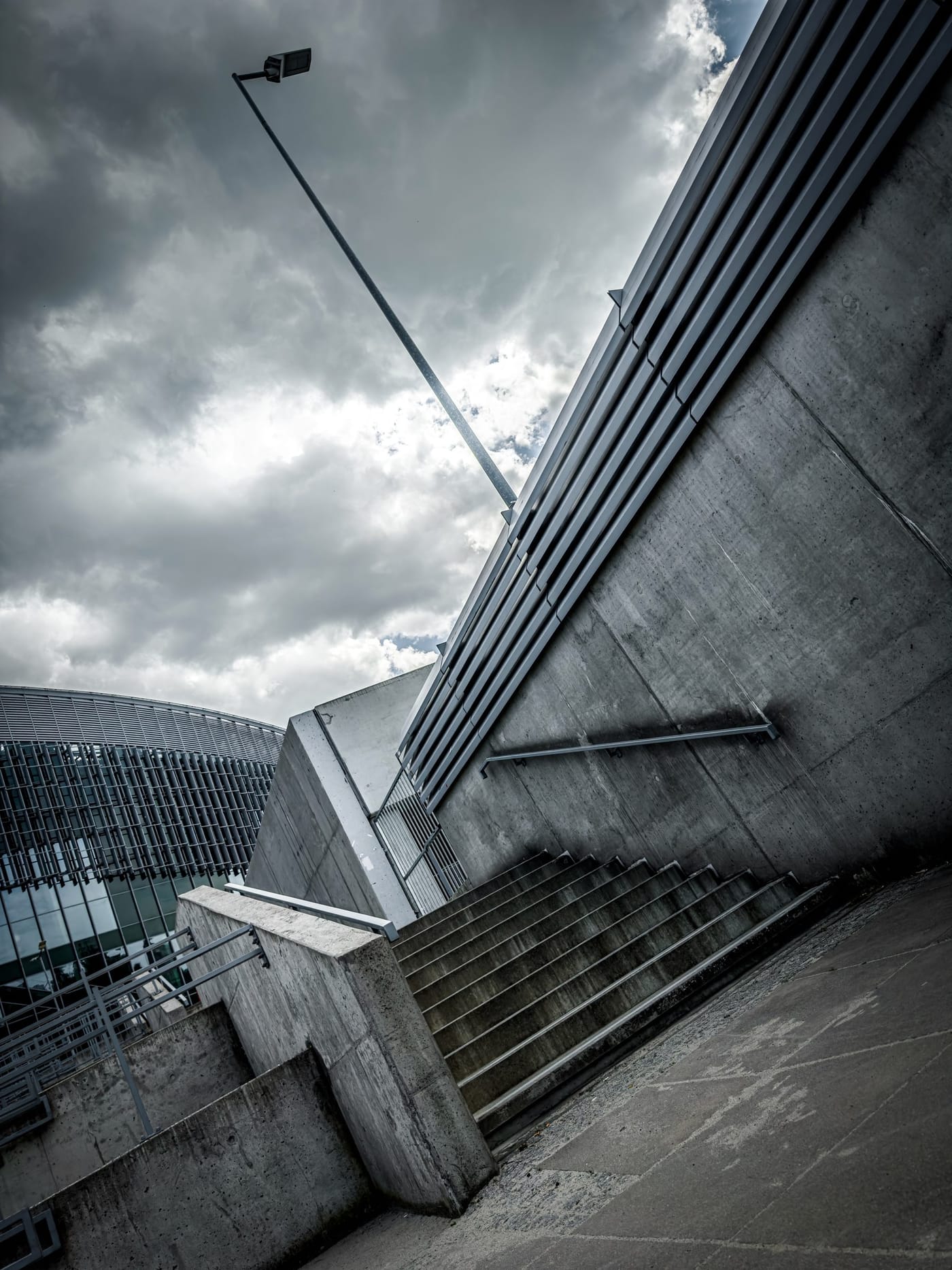 Concrete stairs climbing beside a high concrete wall under a stormy sky