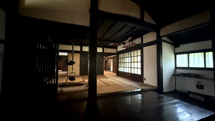 The dark timber interior of an old farmhouse, with light from paper windows