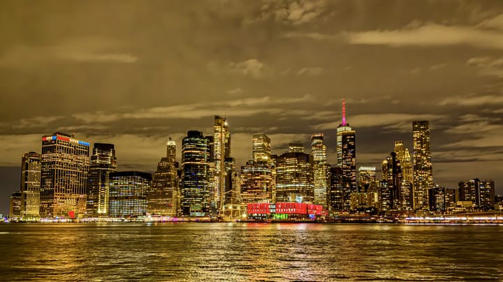 Skyscrapers lit gold at night across a river, reflected in the water