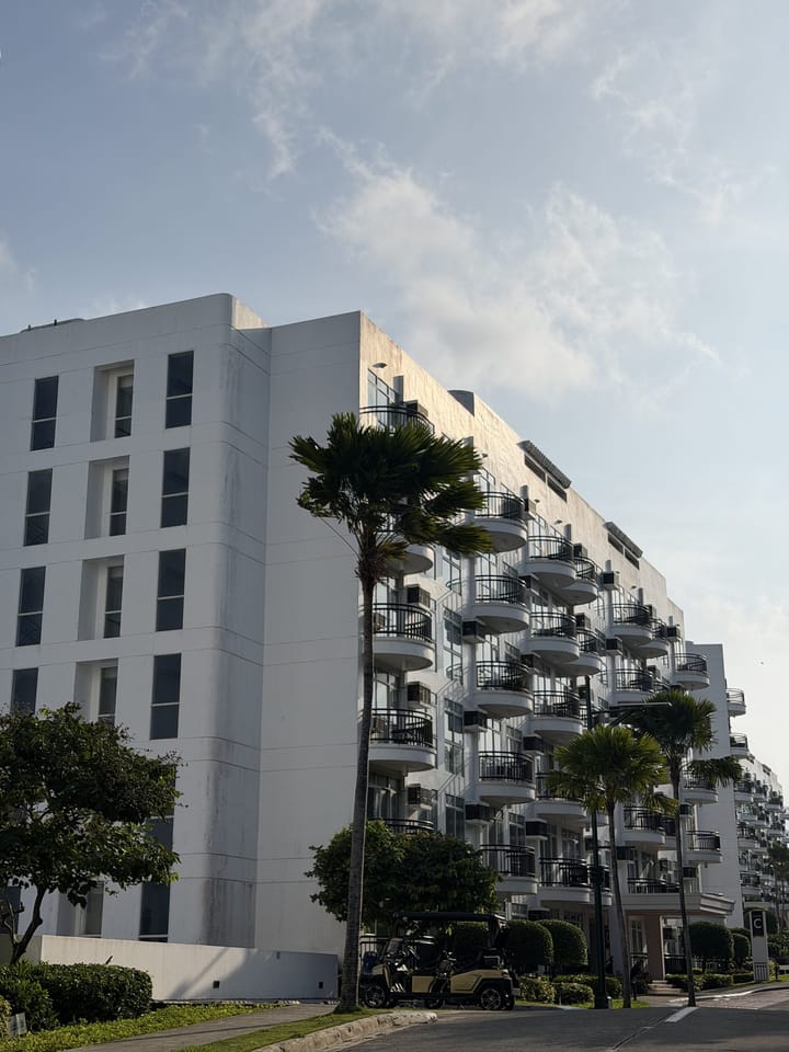 A white apartment block with rows of rounded balconies and palm trees
